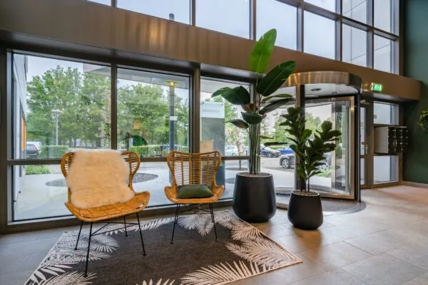 Moderne entree met rotan stoelen, grote planten en een draaideur aan de Baarnsche Dijk.